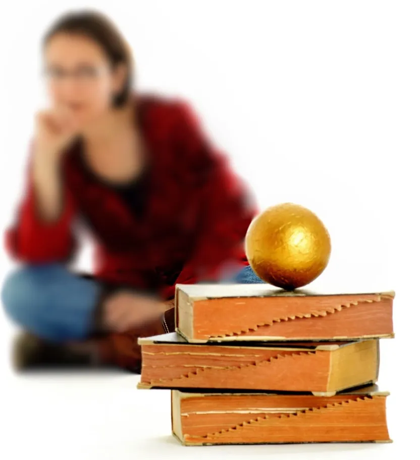 Xenia Busam sitzt unscharf hinter einem Stapel alter Bücher, auf dem eine goldene Kugel liegt
